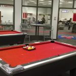 A red pool table with pool sticks leaning against it.