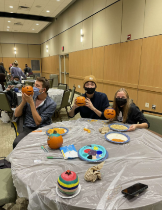 Three people sit at a table and hold up their carved pumpkins